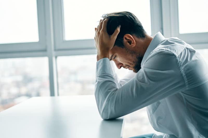 Young man sitting at a table depressed against the background of a window